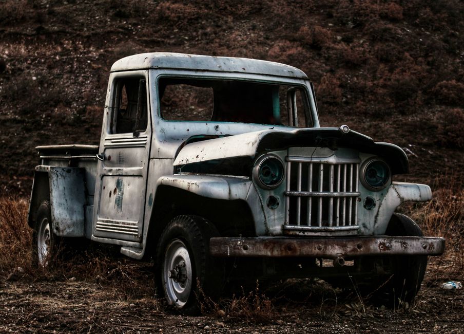 An old, abandoned pickup truck rusting in a dry field.