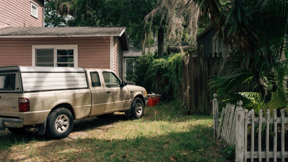 A pick-up truck parked beside a suburban house surrounded by greenery.